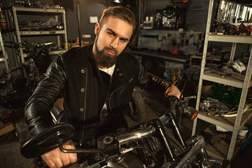 Handsome bearded man on his motorbike at the workshop