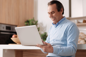 Senior cheerful freelancer using laptop at home