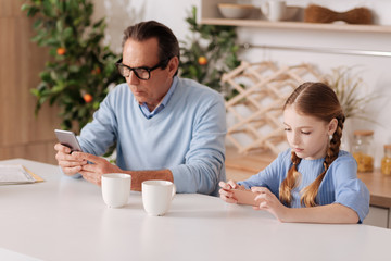 Fototapeta premium Senior grandfather and young granddaughter using smartphones indoors