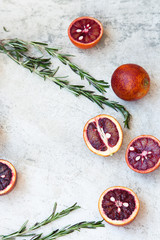 Red Sicilian orange whole and cut on a light background with branches of rosemary. Daylight, open space for your text.