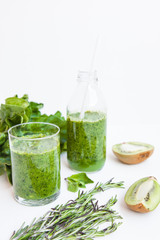 Green cocktail in a bottle and in a glass with spinach, mint, rosemary, kiwi and apple on a light background.