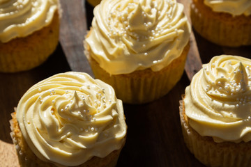 A landscape photo of five delicious cream colored cupcakes on a wooden board.  This image can also be used as a background. 