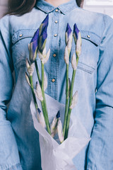 Close-up of a girl in a denim shirt holding a bouquet of unblown flowers iris