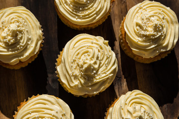 A landscape photo of five delicious cream colored cupcakes on a wooden board.  This image can also be used as a background. 