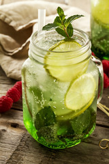 Tasty cold fresh drink lemonade with lemon, mint, ice and lime in glass on wooden table. Closeup.