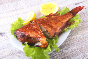 Smoked fish and lemon on green lettuce leaves on Wooden cutting board isolated on white background.