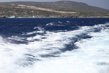 White waves from a yacht on a dark blue sea against the backdrop of the island of Cyprus