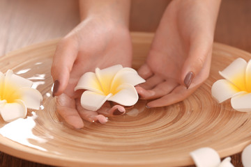Obraz na płótnie Canvas Female hands in spa wooden bowl with flowers, closeup