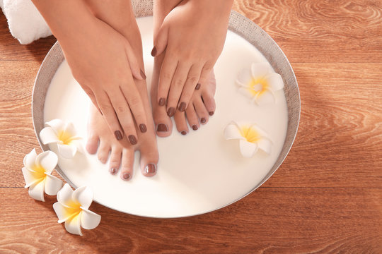 Female feet and hands with brown manicure in spa bowl with milk