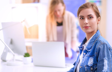 Two young woman standing near desk with instruments, plan and laptop