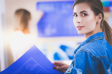 Two young woman standing near desk with instruments, plan and laptop