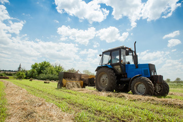 Obraz premium Tractor collects dry hay on the farm field