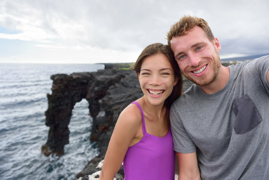 Selfie couple on nature travel Hawaii vacation. Young people taking phone picture at the Holei Sea Arch, tourist attraction on Big Island at the Volcanoes National park.