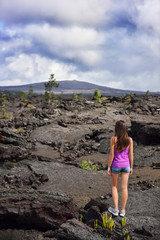 Fototapeta premium Woman hiking in volcanic rocks on volcano of Big island of Hawaii, USA. Tourist hiker walking on volcanic black rocks during summer traveling holidays.