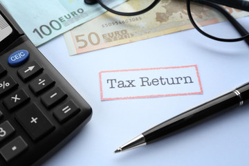 Paper sheet with text TAX RETURN, calculator, pen, spectacles and banknotes on white background, close up