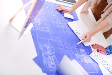 Two young woman standing near desk with instruments, plan and laptop