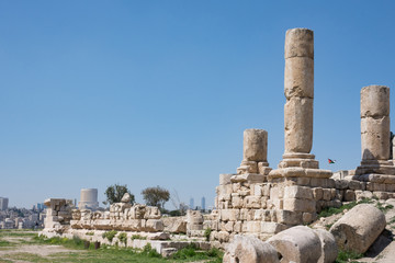 Ancient Roman ruins of the Temple of Hercules at Amman Citadel with a view of Amman city and the Jordanian flag in the background. Fallen blocks are in the foreground.