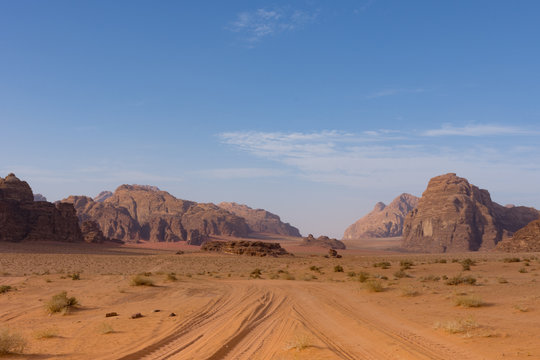 Four wheeling road through orange or rust colored sand with rugged mountains in the distance with deep blue sky above. Photographed in Wadi Rum Desert, Jordan under natural light.