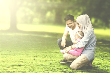 Muslim parents squatting with baby in meadow