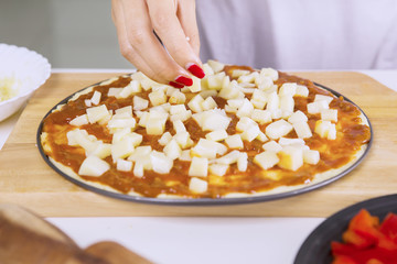 Woman's hand adds slices of cheese to pizza