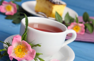Hot tea with cheesecake and wild rose flower on boards