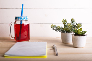 Opened notebook with a cup of tea/fruit-drink and a tiny flower on wooden table. Top view. Writing concept.