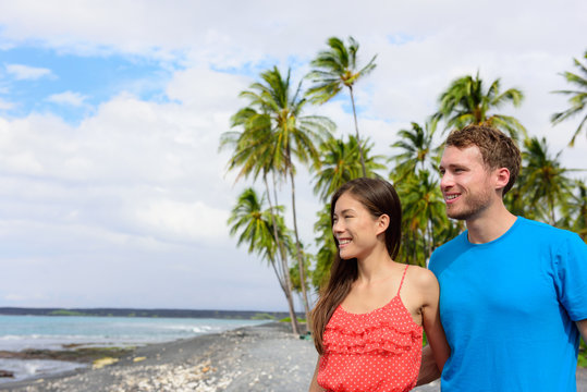 Vacation couple walking holding hands on beach travel destination. Happy summer holidays.black sand beach in Big island of Hawaii, USA.