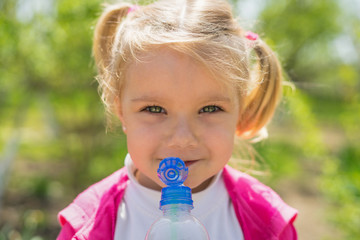 Small cute girl drinking water from plastic bottle. Green sunny photo