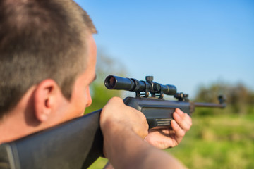 The man takes aim at the target with a sniper strikeball rifle. Selective Focus. Blue sky.