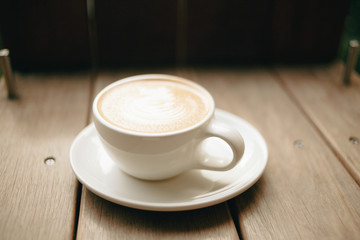 Cafe latte in a white coffee cup and plate on a wooden table