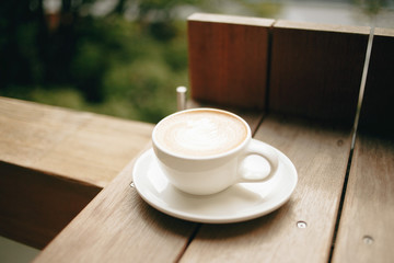 Cafe latte in a white coffee cup and plate on a wooden table