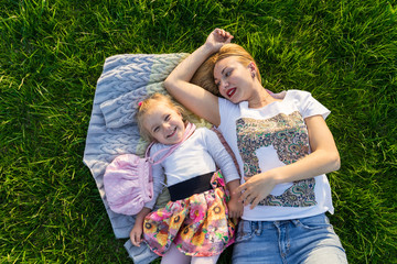 Happy Mother and daughter smiling at the park having picnic. They are lying and resting on green lawn with grass