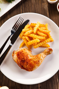 Roast chicken leg with french fries on wooden table