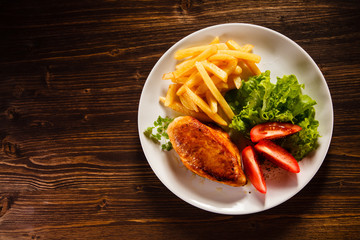 Grilled chicken fillet with french fries on wooden table