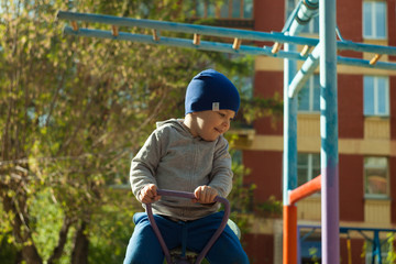 Little toddler boy on a swing balance on the kid playground. He is playing seesaw and laughing in a park in the city. The idea of education and health. Children energetic and intelligent.