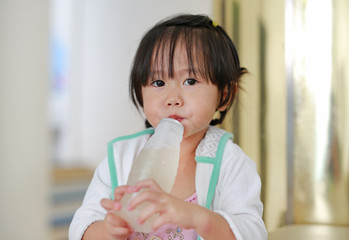 Cute little girl using straw to drink honeydew from bottle.