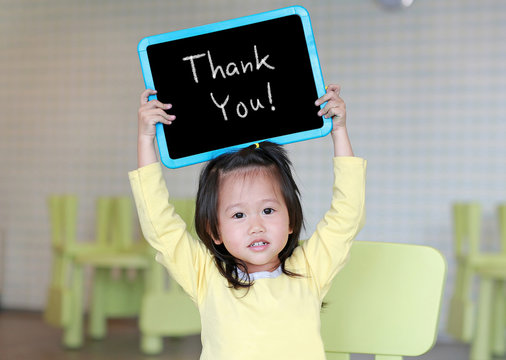 Cute little child girl holding blackboard showing text " Thank You " in kids room. Education concept.