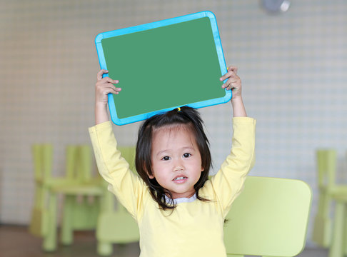 Cute asian child girl holding empty green blackboard in kids room.