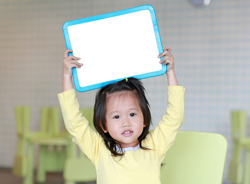 Cute asian child girl holding empty white blackboard in kids room.