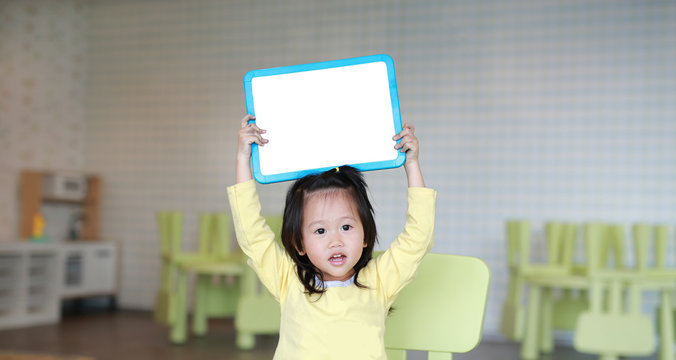 Cute asian child girl holding empty white blackboard in playroom.