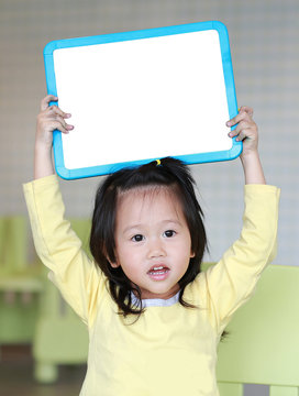 Cute asian child girl holding empty white blackboard in playroom.