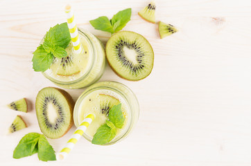 Fototapeta na wymiar Decorative frame of green kiwi fruit smoothie in glass jars with straw, mint leaf, cute ripe berry, top view. White wooden board background, copy space.