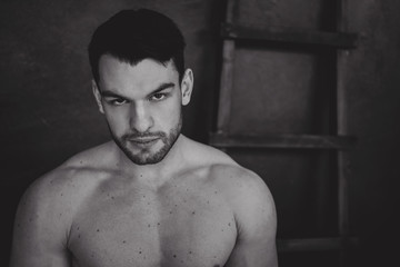 Portrait of young attractive man with muscular strong black beard, piercing sexy look in the studio posing