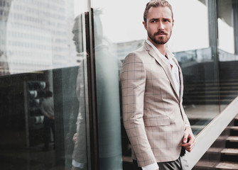 portrait of sexy handsome fashion male model man dressed in elegant beige checkered suit .posing on the street background