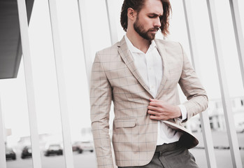 portrait of sexy handsome fashion male model man dressed in elegant beige checkered suit .posing on the street background