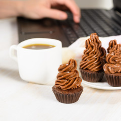 Young woman eat cupcakes with coffee and working at laptop
