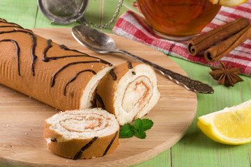 Biscuit swiss roll with a cup of tea on green wooden background