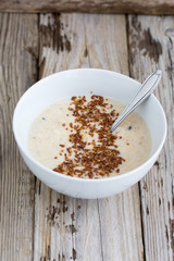 Fresh cooked oatmeal porridge with crushed linseed. On wooden table. Natural light, selective focus. 