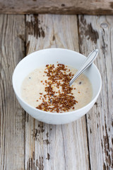 Fresh cooked oatmeal porridge with crushed linseed. On wooden table. Natural light, selective focus. 