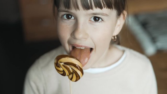 Portrait of teenager brunette girl eatsing big candy and smiling to camera, indoors shot